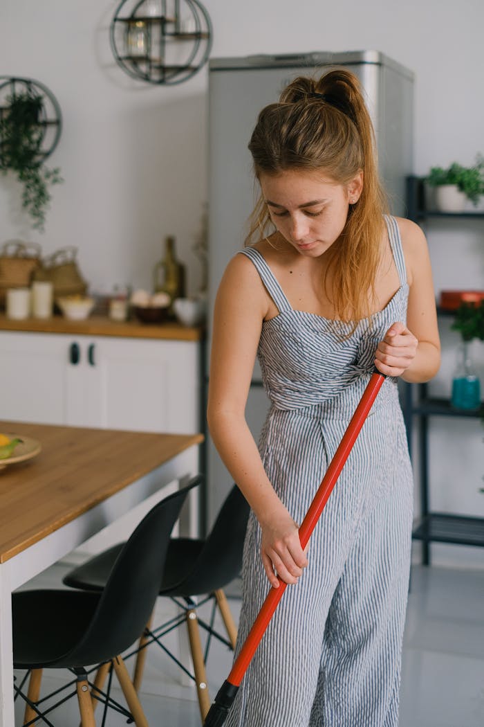 A young woman mopping the floor in a stylish and modern kitchen setting.